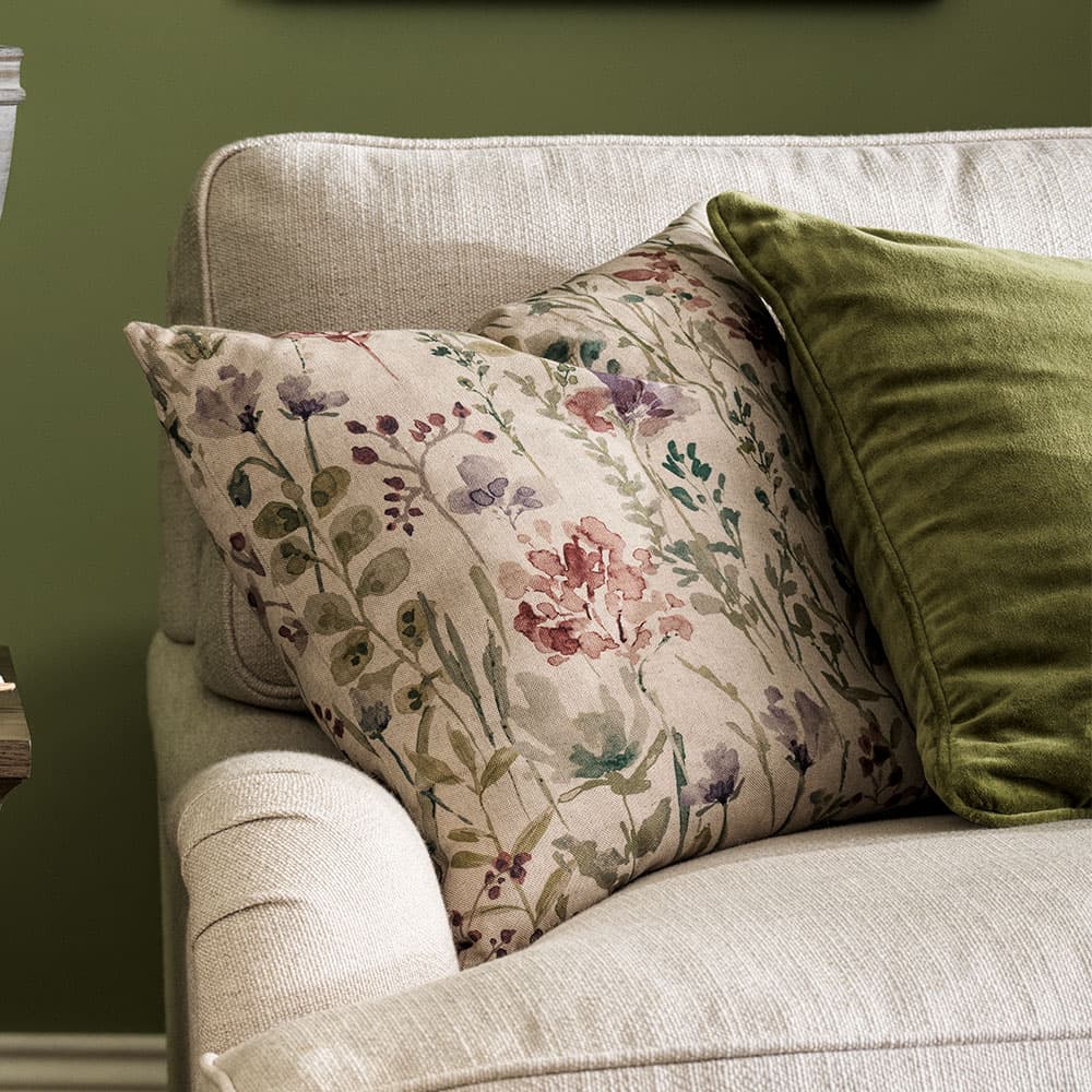 Floral and green cushions on a beige sofa against a green wall, creating a cozy and inviting atmosphere.