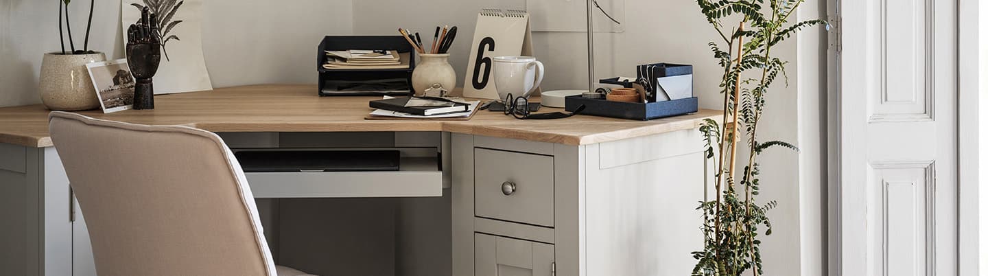 A cozy home office with a wooden desk, organized stationery, a potted plant, a cushioned chair, and natural light from a nearby window.