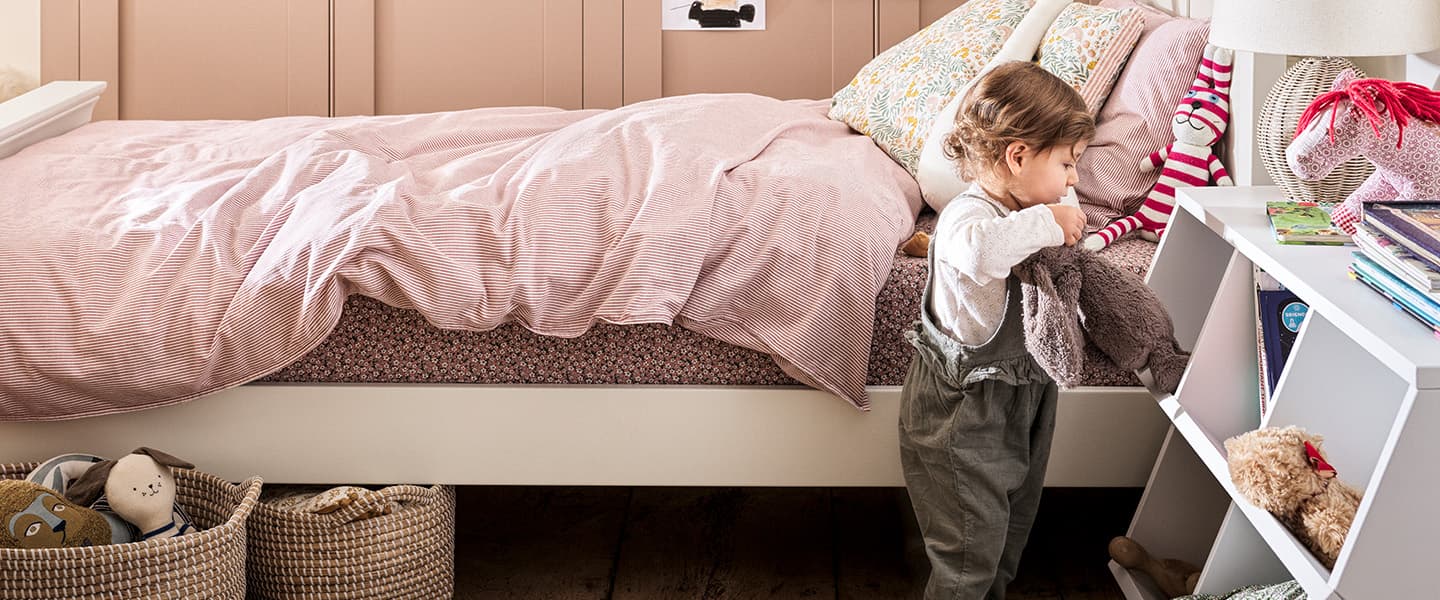 Children's bedroom with soft pink bedding and toddler going through toys