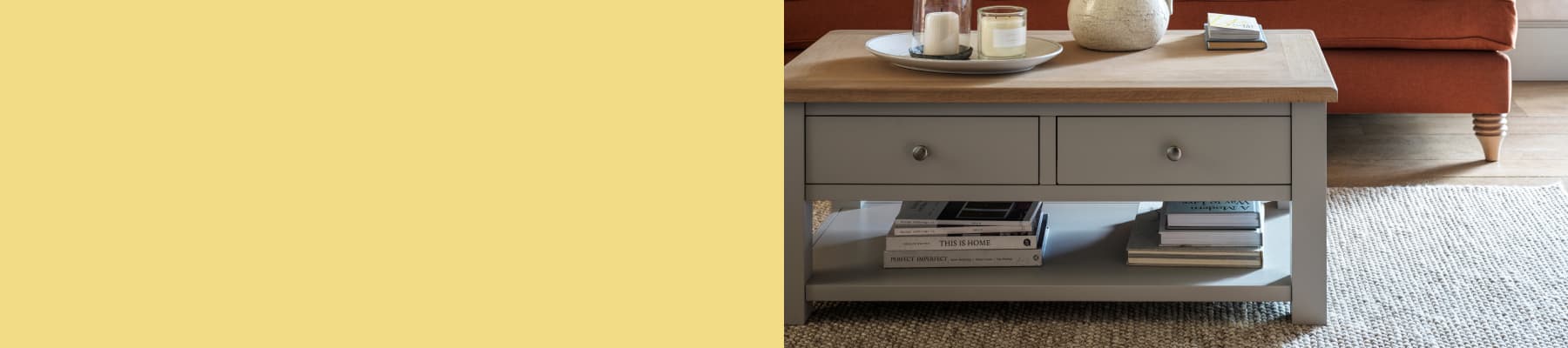 Painted coffee table wooden top and two drawers, books on the lower shelf, and candles on top, next to an orange sofa and a beige rug.