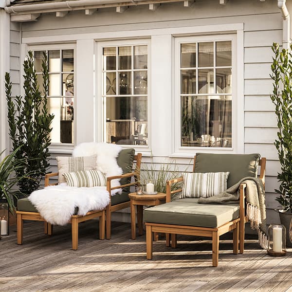 Outdoor seating area with wooden lounge chairs and green cushions, white throw, and plants on a wooden deck.