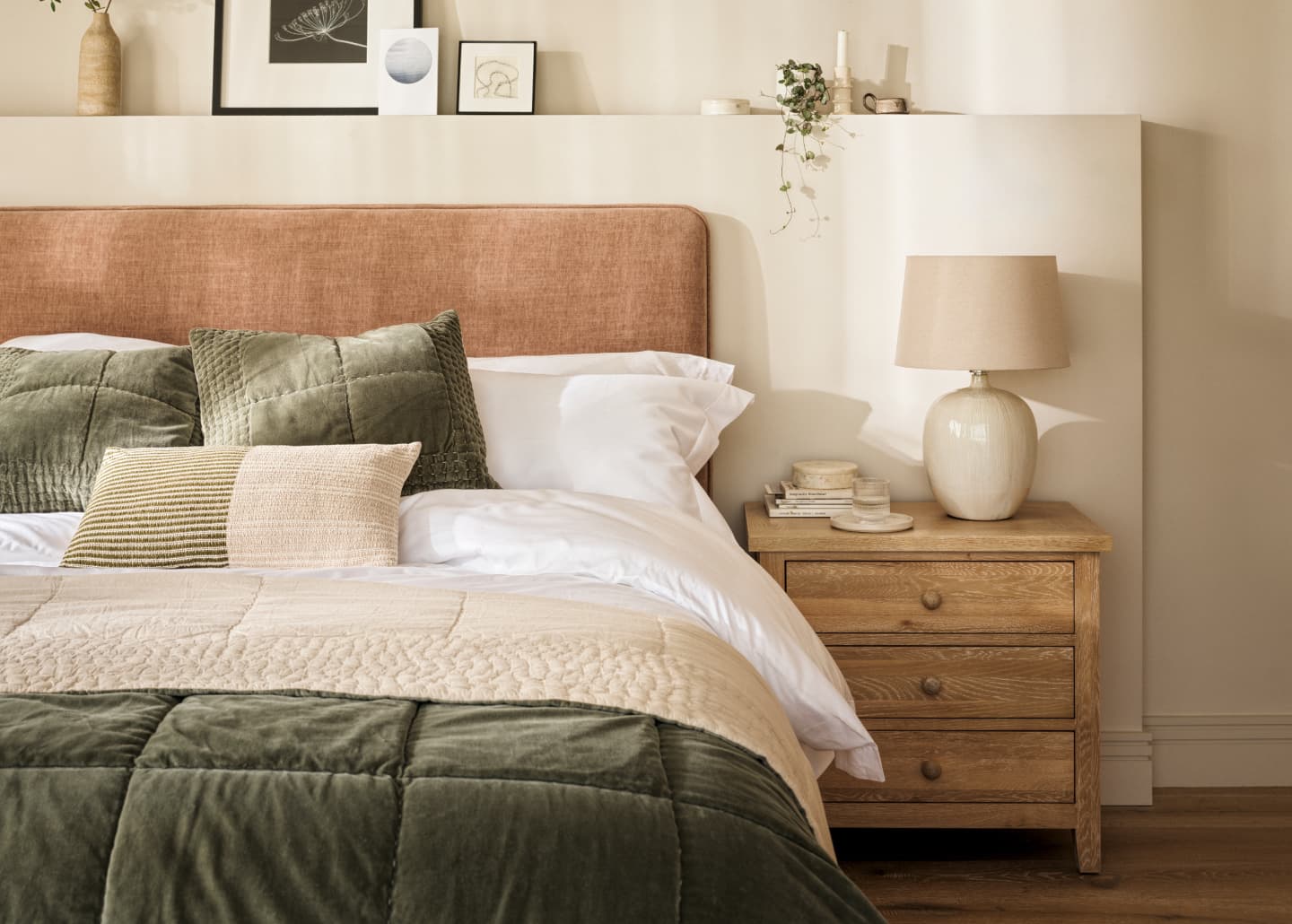 Inviting bedroom with a upholstered headboard, green and beige bedding, a wooden nightstand, and decorative art on the wall.