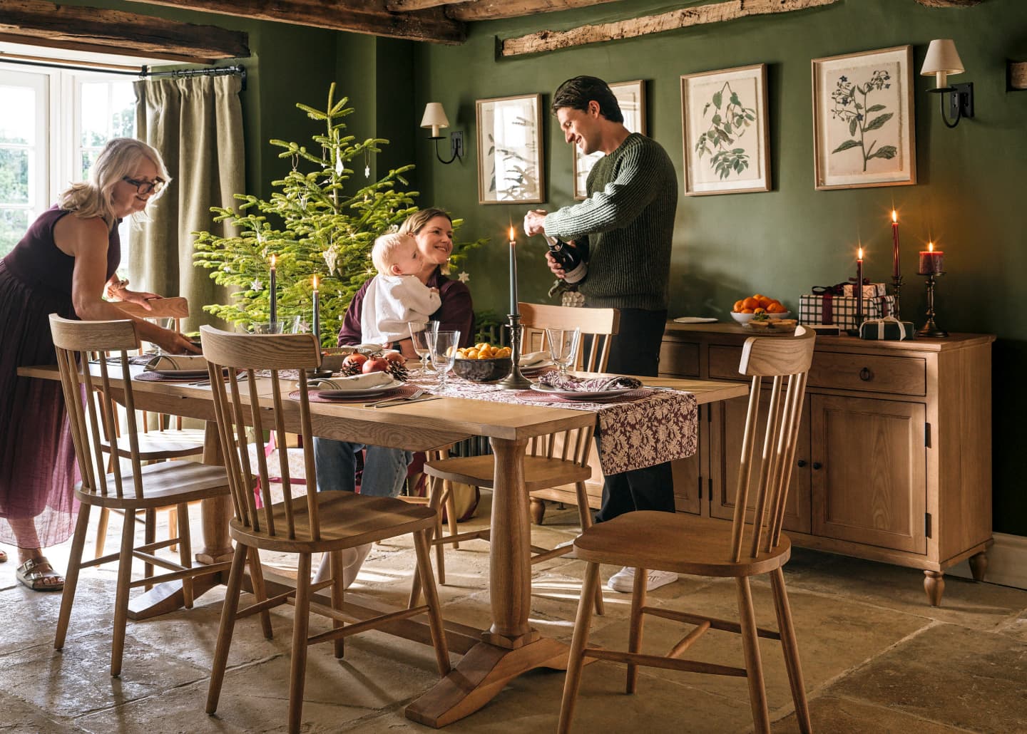 Family gathering in a cosy dining room with holiday decorations, a small Christmas tree, and a table set for dinner.