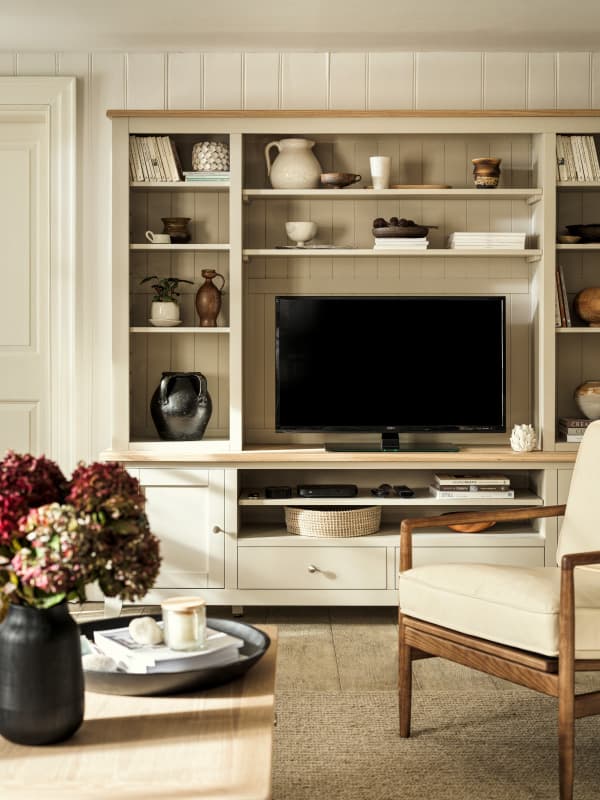 TV within a large beige coloured media unit with an accent chair and a coffee table in the foreground.