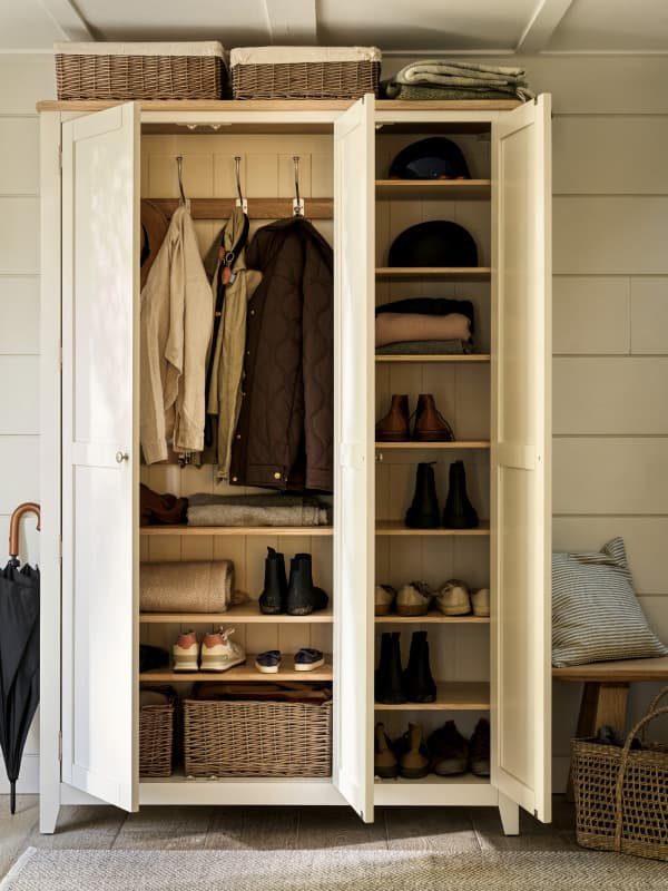 A neatly organized wardrobe with coats, bags, and shoes. Shelves hold hats, baskets, and folded clothes. An umbrella stands nearby.