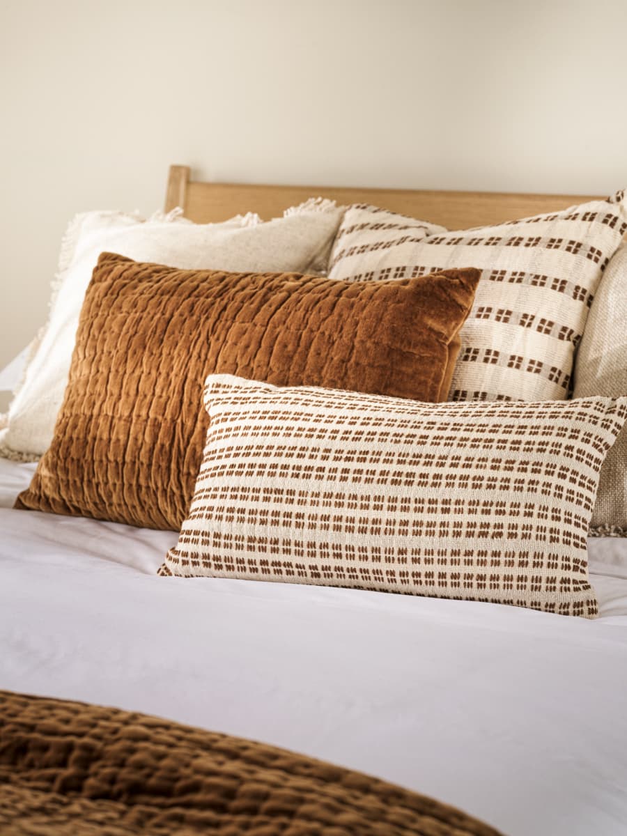 A bed with multiple pillows featuring earthy tones and textured fabrics, including a brown velvet pillow and patterned cushions.