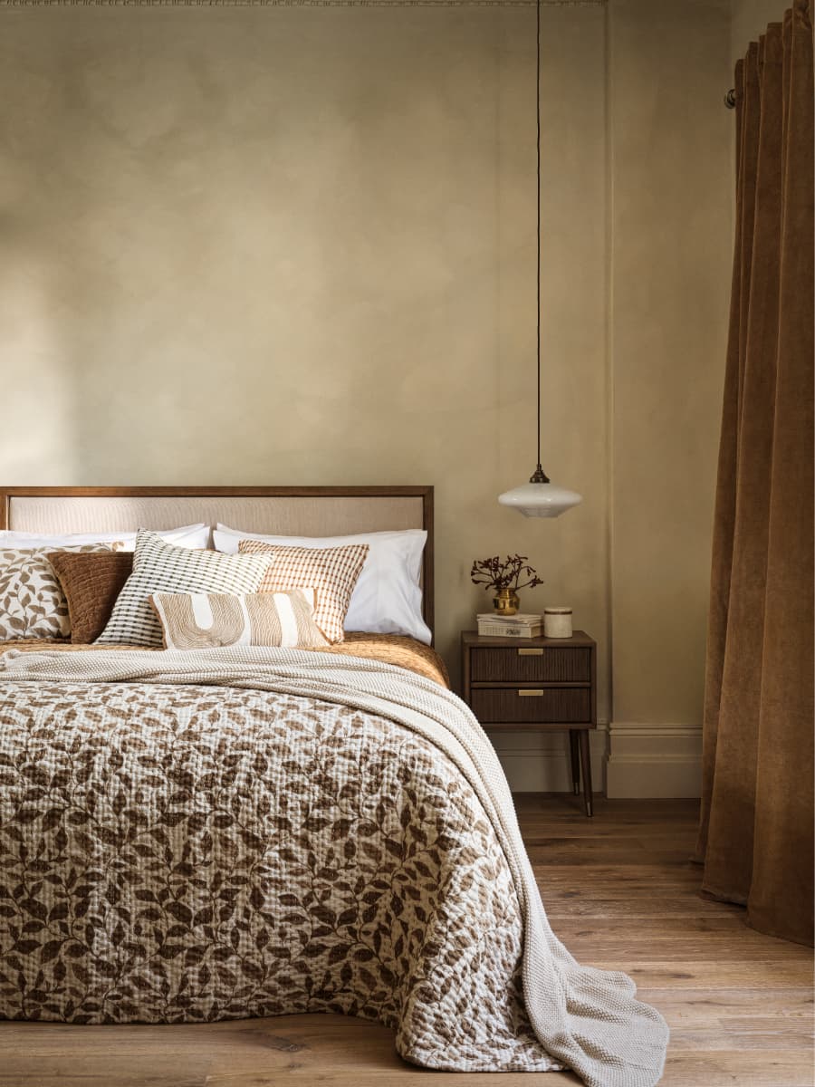 Cosy bedroom with a patterned quilt, multiple pillows, a small bedside table, and a hanging light fixture, offering a warm, inviting atmosphere.