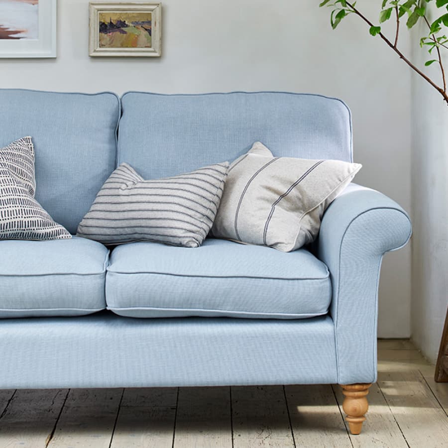 Light blue sofa with striped and patterned cushions against a white wall, wooden floor, and framed artwork.