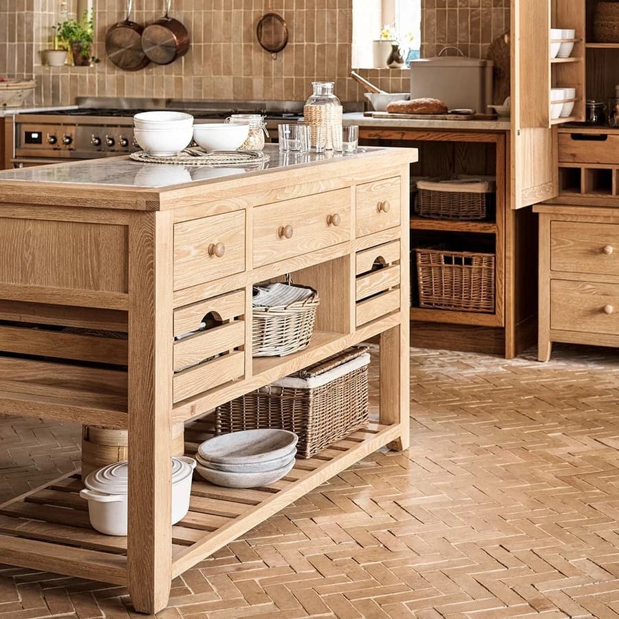 Rustic kitchen with a wooden island, open shelves, baskets, and a tiled floor. Pots and bowls are neatly placed on the island counter.