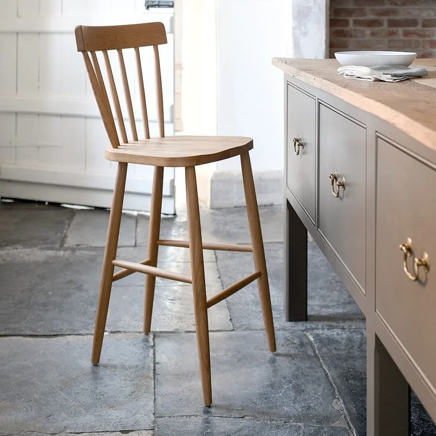 Wooden bar stool with a slatted back next to a kitchen island in a rustic kitchen with stone flooring.